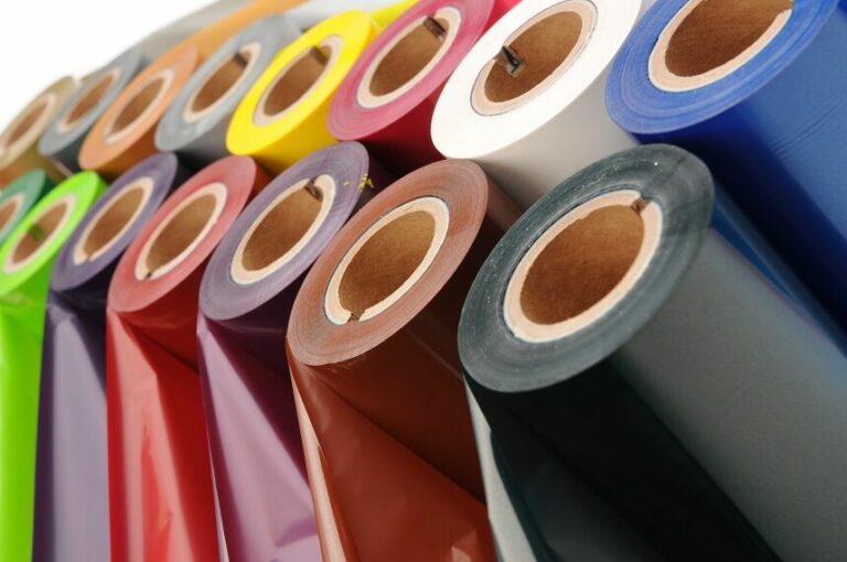 A vibrant collection of colorful vinyl rolls—green, red, purple, yellow, pink, blue, gray, white, and black—are arranged upright in close proximity, perfect for adding a splash of color to any home project.
