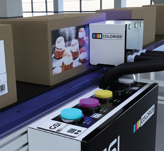 A conveyor system prints colored images of pastries on cardboard boxes using a device labeled "COLORIZE," seamlessly integrating both coding and marking functionalities.
