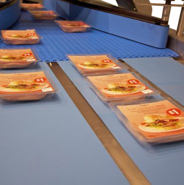Plastic containers with packaged sliced meat move efficiently on a conveyer belt in a food processing facility, showcasing process improvement in action.