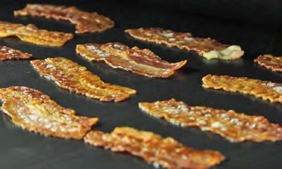 Several crispy bacon strips frying on a black surface, showcasing the delicious art of food processing.