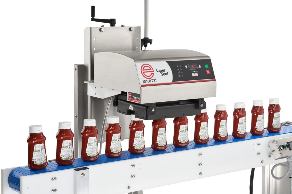 Conveyor belt with ketchup bottles moving under a machine labeled "Super Seal.